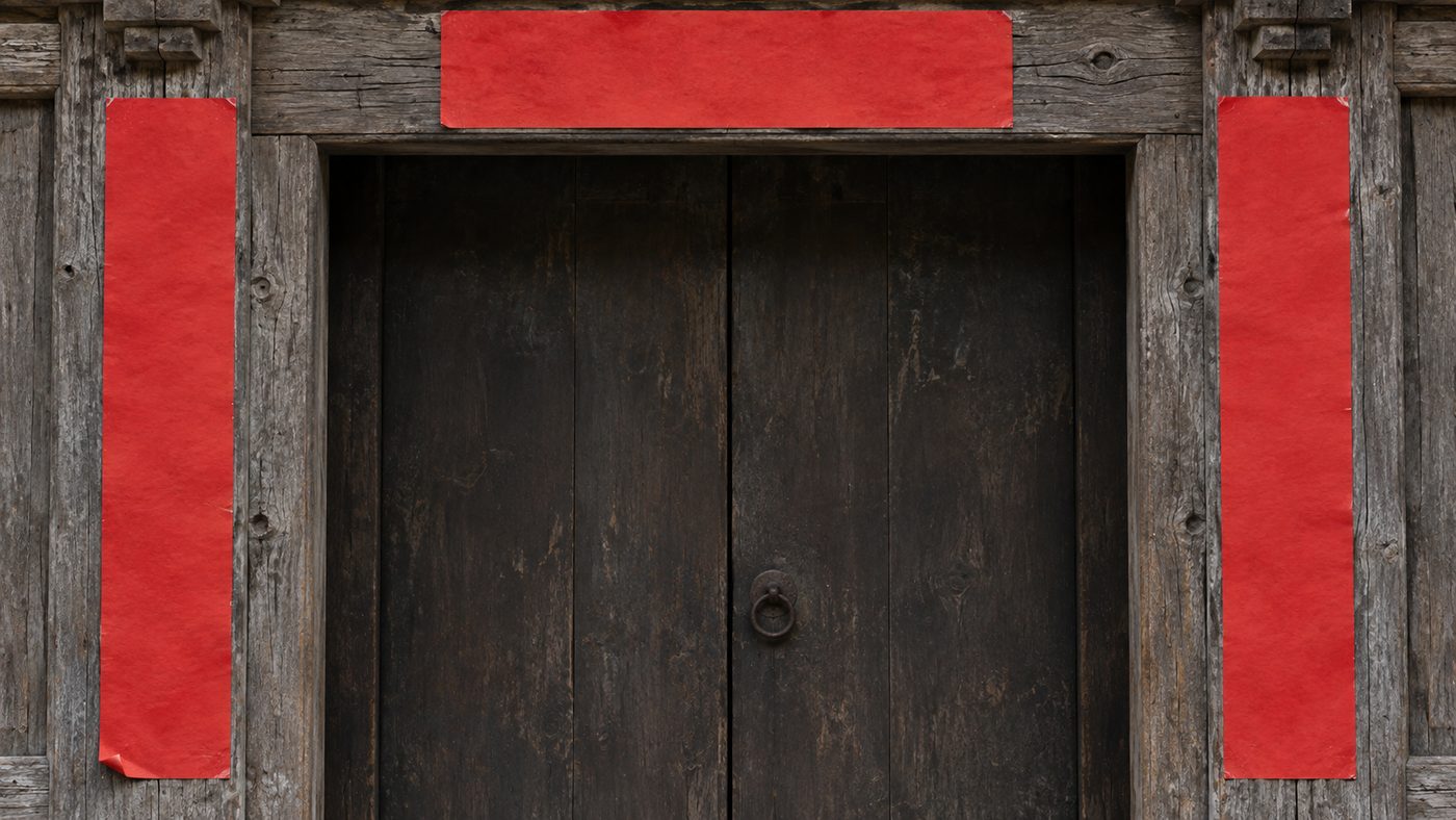 A weathered red door frame with a fresh strip of red paper pasted down each side and one across the top, gold characters brushed on them, seen straight on in flat daylight.