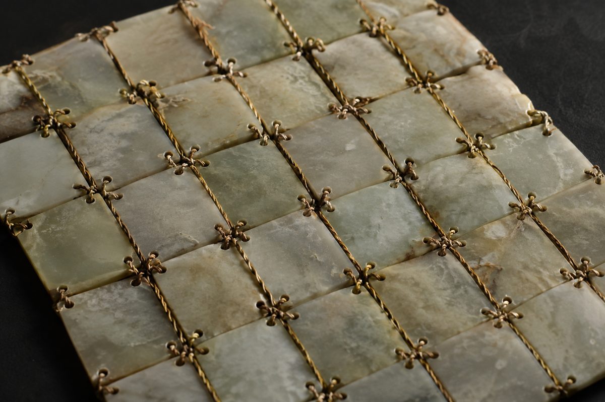 An illustration of a fragment of a jade burial case: rectangular jade plaques laid edge to edge and stitched at their drilled corners with fine twisted gold wire.