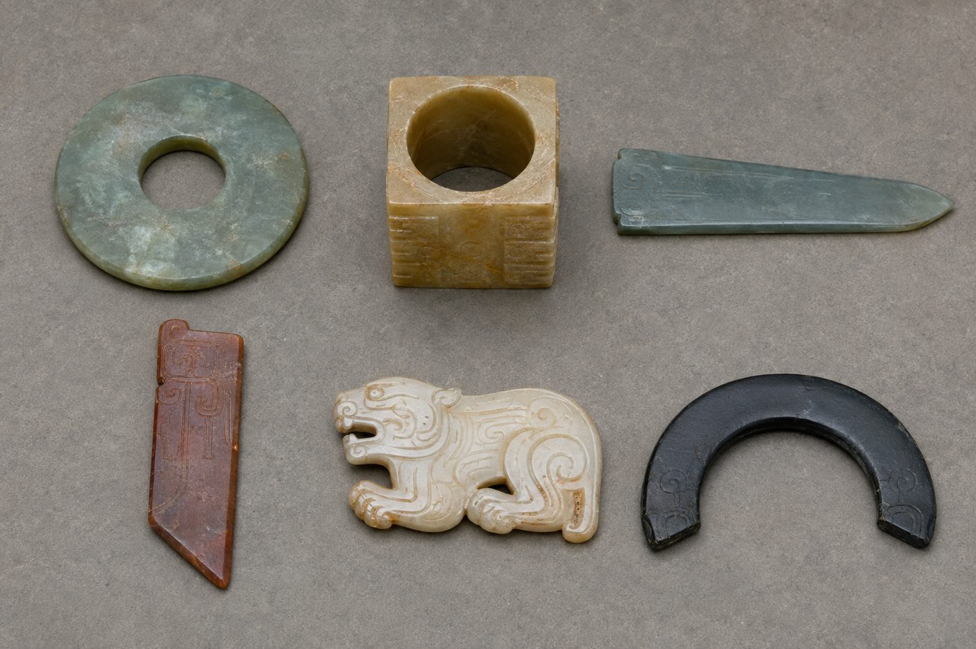 An illustration of the six ritual jades laid out in two rows: a green disc, a yellow square tube, a blue pointed tablet, a red angled tablet, a white tiger plaque, and a black half-ring.